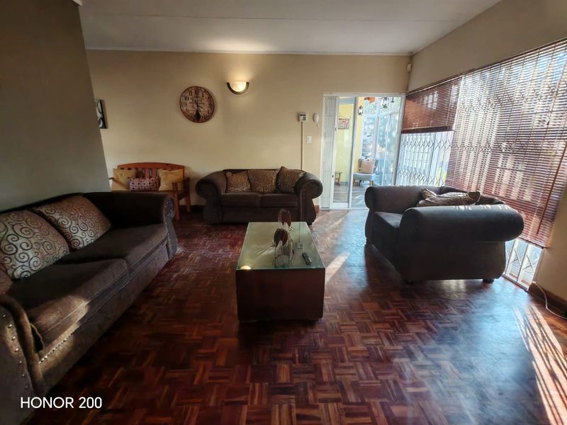 Spacious living room featuring classic parquet flooring, natural light through large windows with venetian blinds, and direct access to an outdoor patio area.