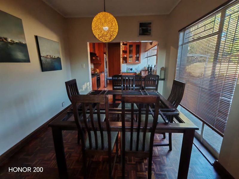 Dining room featuring parquet flooring and venetian blinds, with an open-plan view into the adjacent kitchen area.