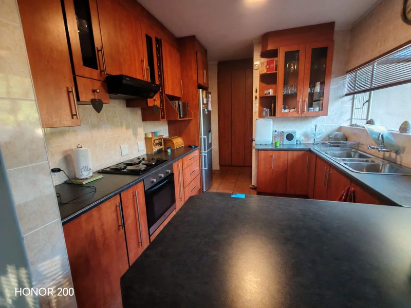 A functional kitchen featuring warm-toned wooden cabinetry, dark laminate countertops, a built-in oven, hob, and a double sink with tiled backsplash.
