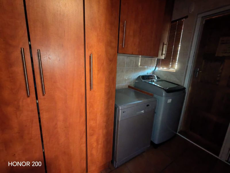 A functional laundry area featuring built-in wooden cabinetry, tiled backsplash, and space for appliances.