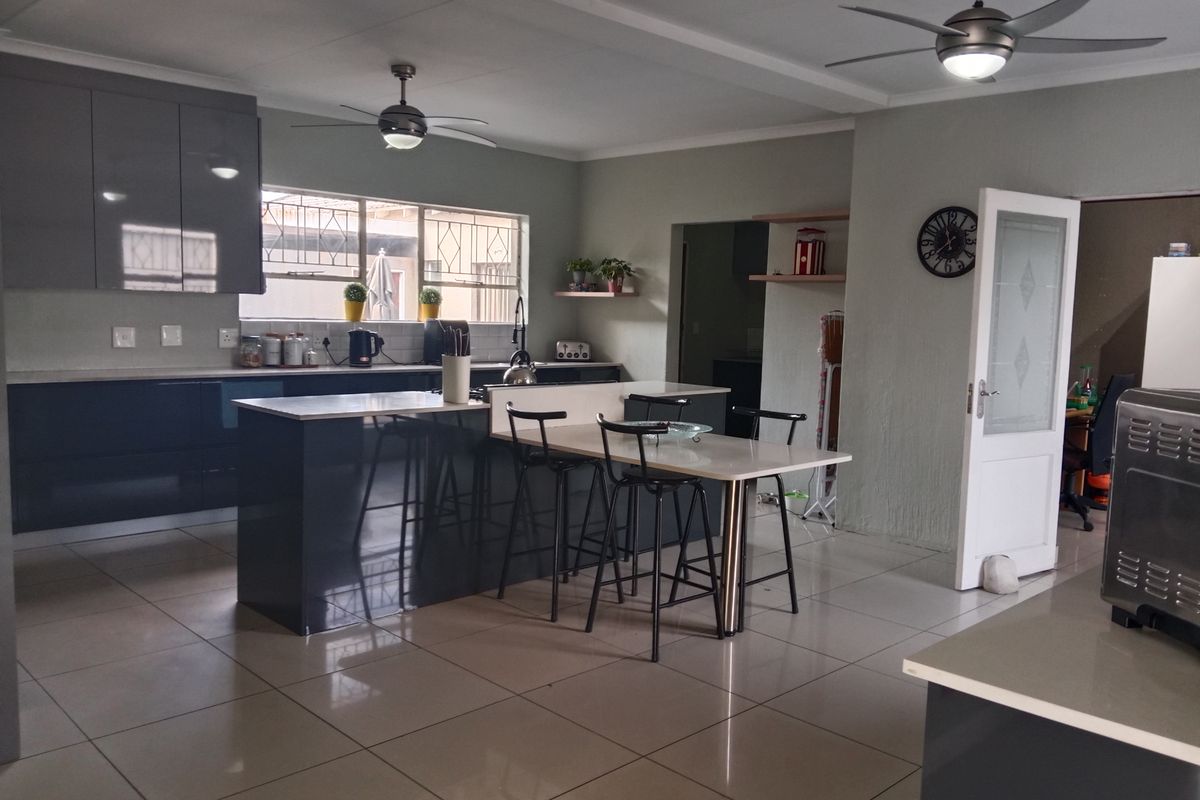 Modern open-plan kitchen featuring sleek glossy cabinetry, a central island with an integrated breakfast bar, and neutral tiled flooring throughout.