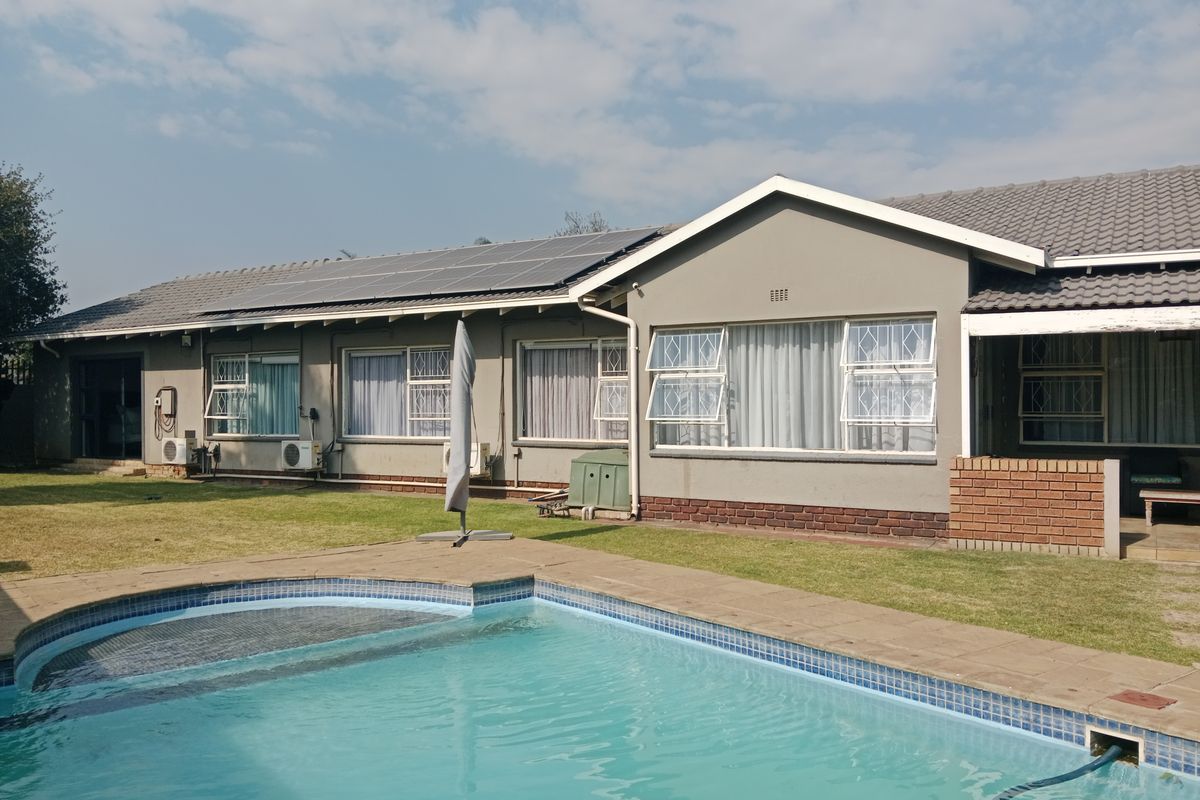Rear view of the house featuring a swimming pool, solar panel installation on the roof, and a well-maintained lawn area.