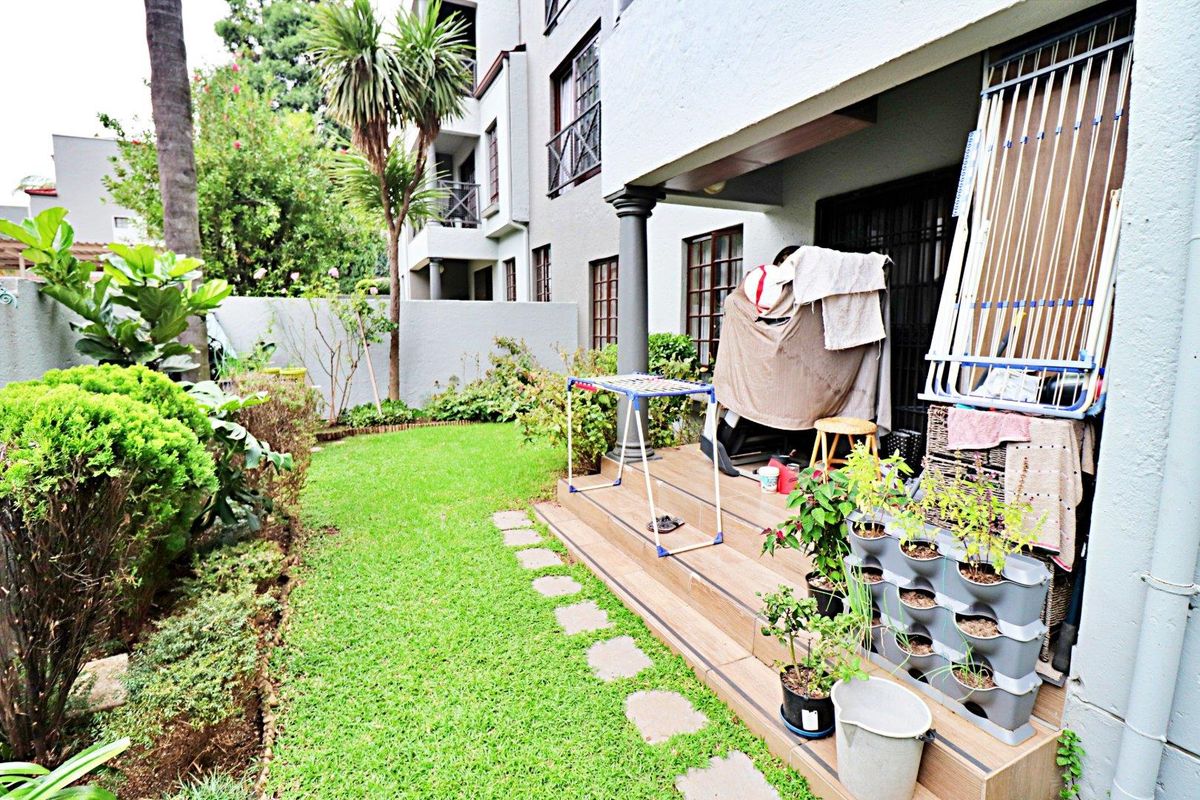 A rear townhouse patio featuring tiled flooring and a small private garden area with a lawn and boundary wall.