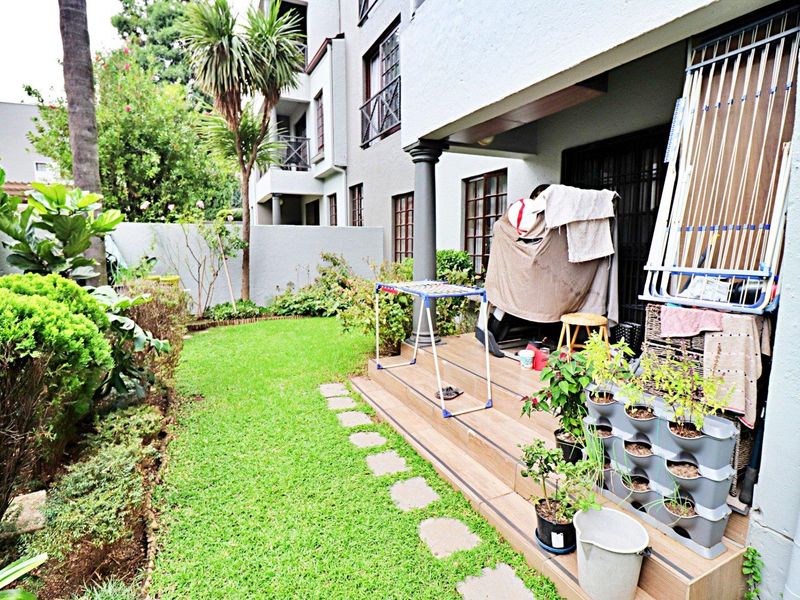 A rear townhouse patio featuring tiled flooring and a small private garden area with a lawn and boundary wall.