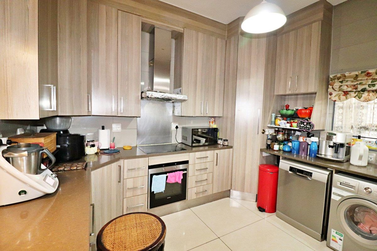 A well-maintained kitchen featuring modern wood-finish cabinetry, stone countertops, built-in oven and hob, and integrated dishwasher with tiled flooring.