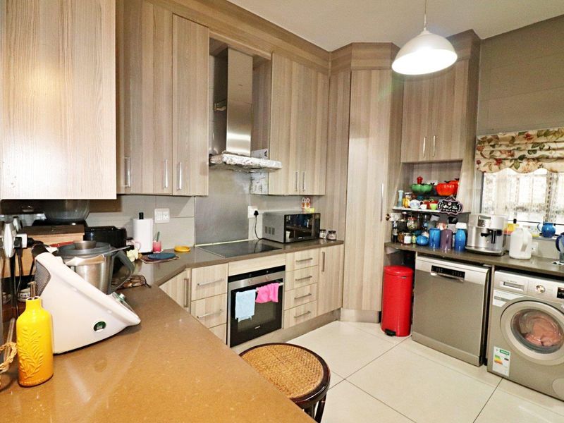 Functional kitchen featuring light wood-grain cabinetry, stone countertops, built-in oven and hob, and dedicated space for laundry and dishwashing appliances.