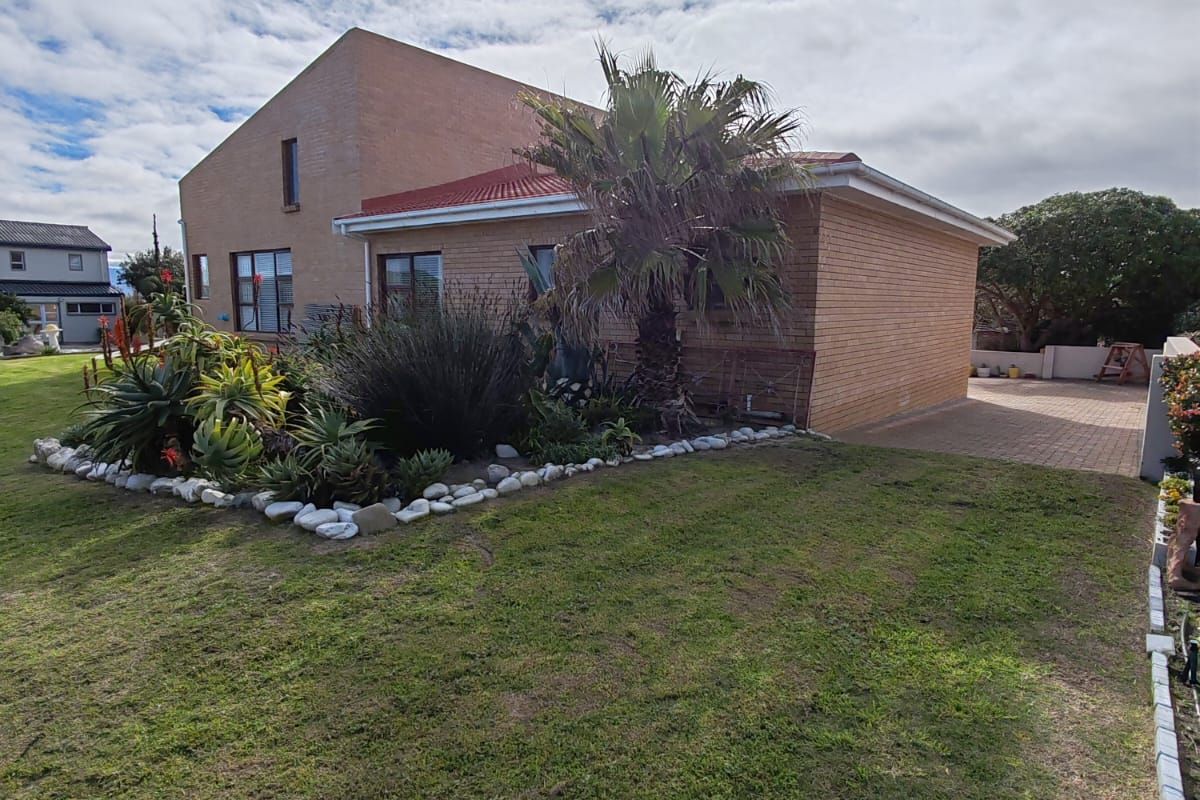A view of the rear exterior of the house featuring a brick facade, tiled roof, paved driveway, and a well-maintained garden area.