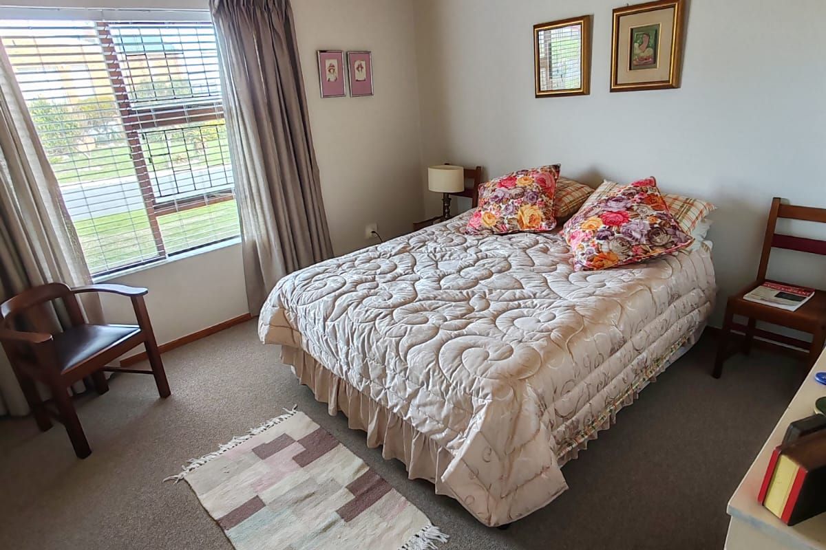 A bedroom featuring a timber tongue and groove ceiling, carpeted flooring, and an aluminium window frame with blinds.