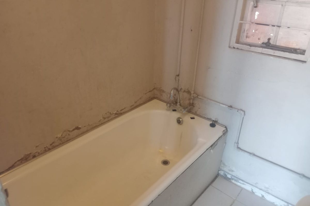 A dated bathroom featuring a bathtub with exposed plumbing and significant wall finish deterioration, requiring renovation and cosmetic updates.