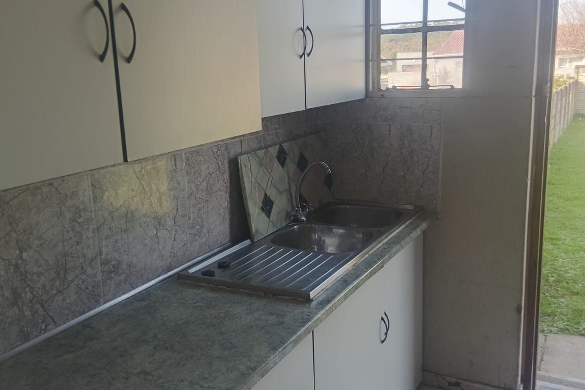 A compact kitchen featuring laminate countertops, a stainless steel sink, tiled backsplash, and built-in cabinetry with direct access to the rear garden.