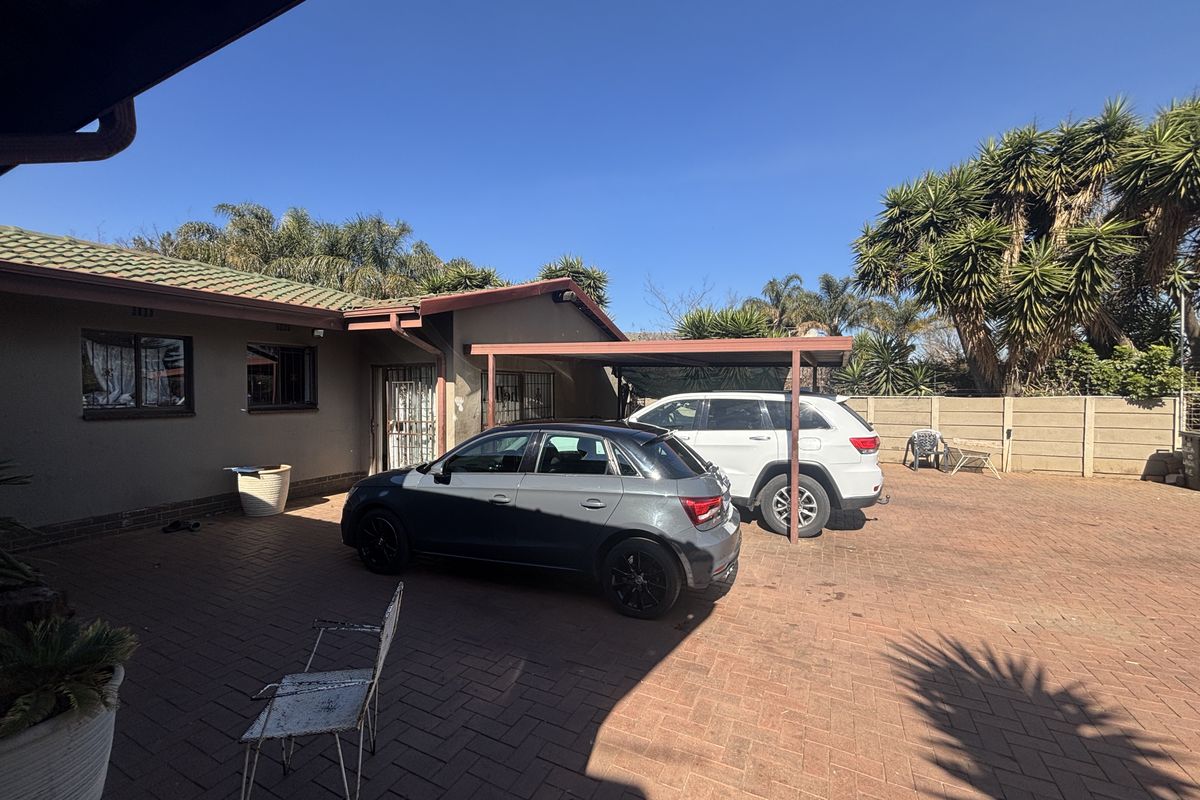 Rear exterior view of the property featuring a paved driveway, a covered carport, and a secure boundary wall.