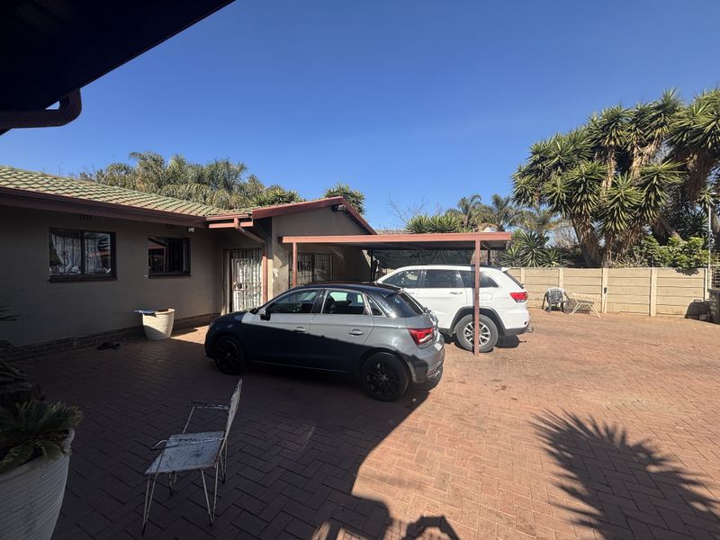 Rear exterior view of the property featuring a paved driveway, a covered carport, and a secure boundary wall.