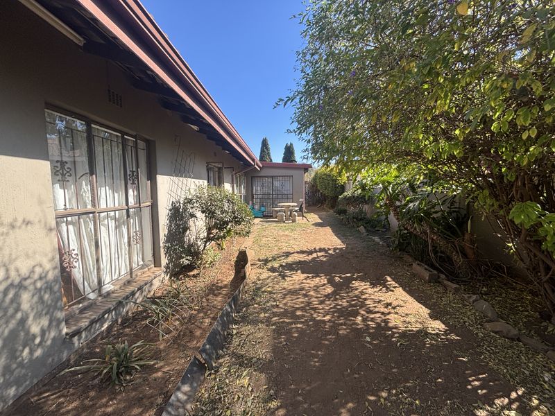 A view of the rear exterior of the house featuring a side pathway, security gates, and established garden area.
