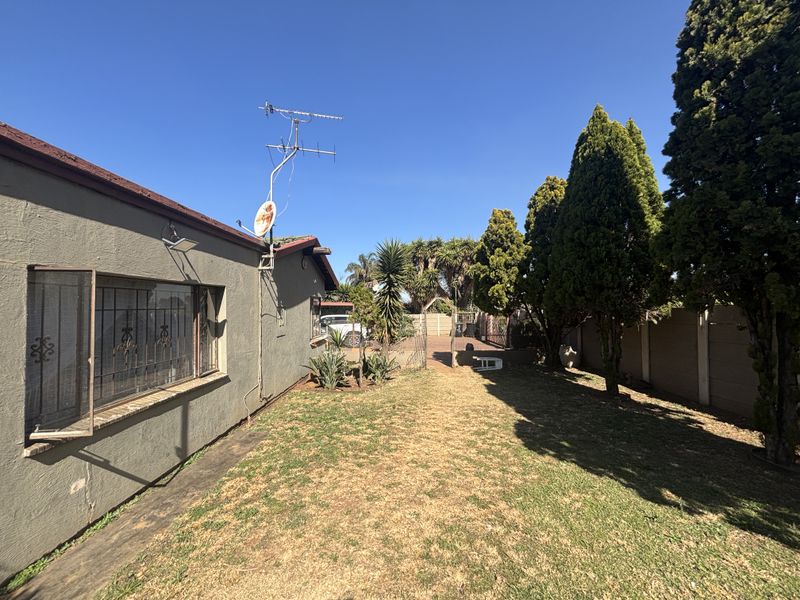 A view of the rear garden featuring a lawn, perimeter precast concrete walling, and the side elevation of the house with security bars.