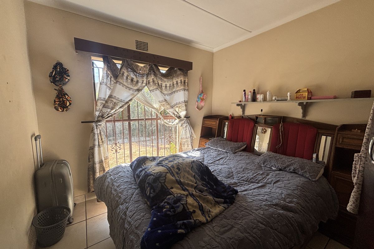 A bedroom featuring tiled flooring, a security gate on the window, and a wall-mounted shelf, requiring cosmetic updates to improve its overall condition.
