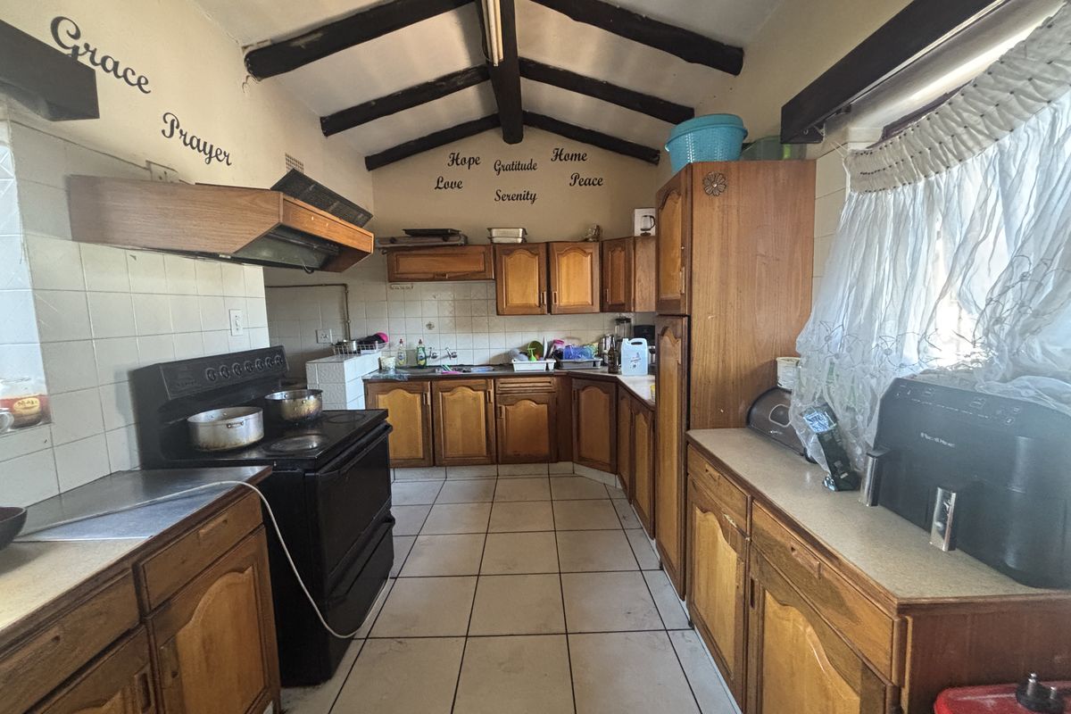 A dated kitchen featuring wooden cabinetry, exposed timber ceiling beams, and tiled flooring, offering a functional layout with significant potential for modernization.