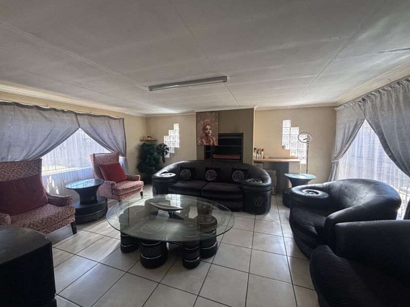A spacious living room featuring ceramic floor tiles, glass block windows, and a central ceiling light fixture.