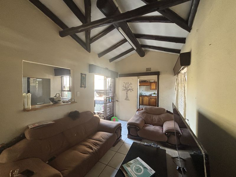 Living room featuring exposed timber ceiling beams, tiled flooring, and a convenient pass-through window connecting to the kitchen area.