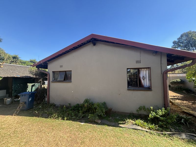 Rear exterior view of the house showing the roofline, gutters, and window security features set against a garden area.
