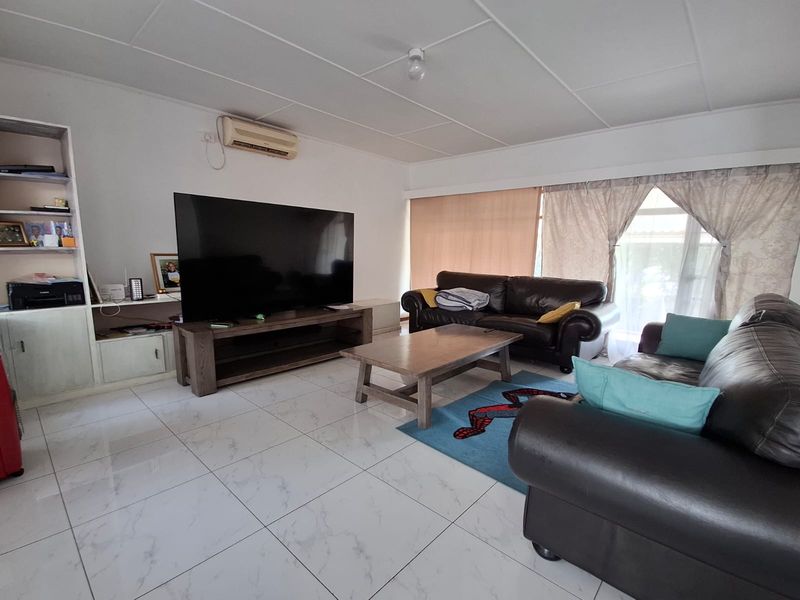 A spacious living room featuring large format floor tiles, a built-in shelving unit, and a wall-mounted air conditioning unit.