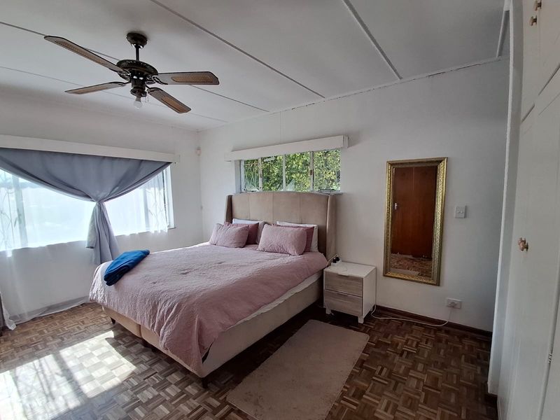 A well-lit bedroom featuring classic parquet flooring, a ceiling fan, and built-in storage cupboards.