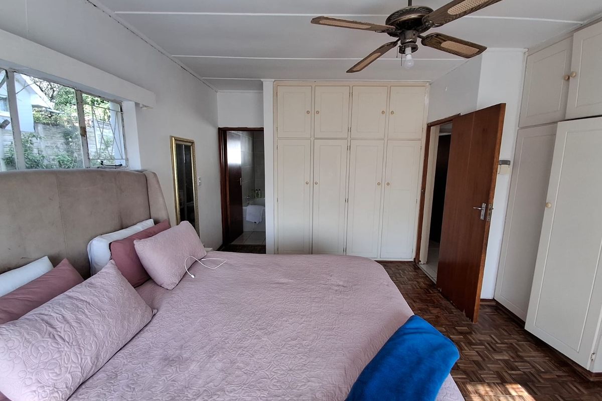 A bedroom featuring classic parquet flooring, extensive built-in cabinetry, and a ceiling fan, offering a functional space with potential for modern updates.