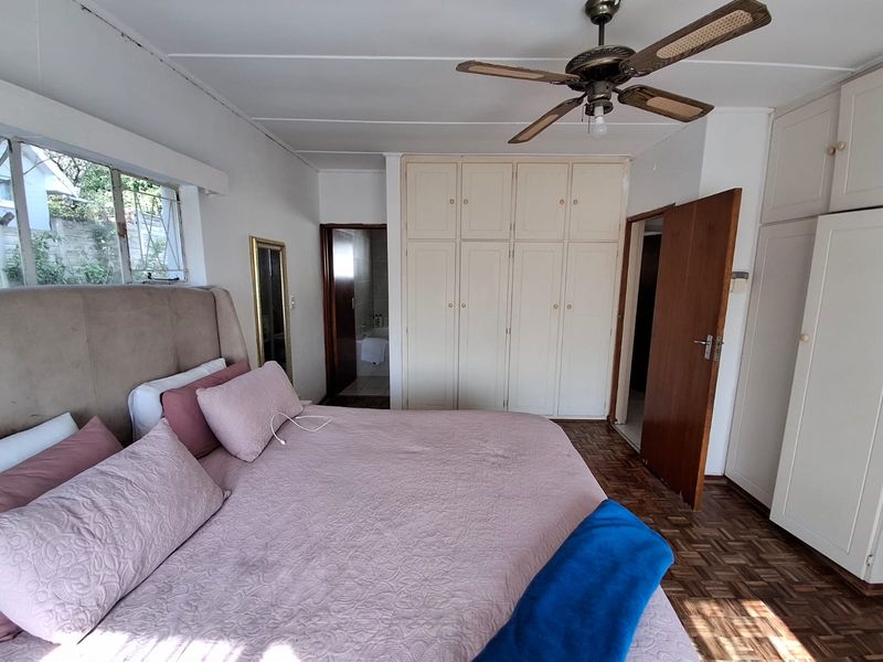 A bedroom featuring classic parquet flooring, extensive built-in cabinetry, and a ceiling fan, offering a functional space with potential for modern updates.