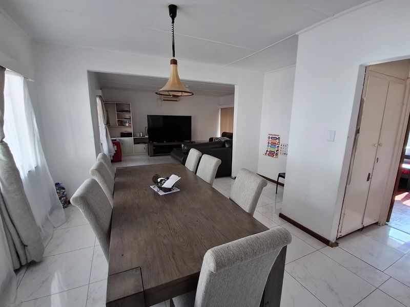 Open-plan dining and living area featuring tiled flooring, neutral walls, and a central pendant light fixture, creating a functional and connected living space.