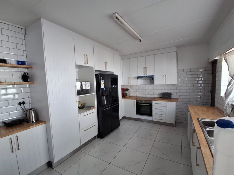 Modern kitchen featuring white cabinetry, subway tile backsplash, wooden countertops, built-in oven, extractor fan, and tiled flooring.