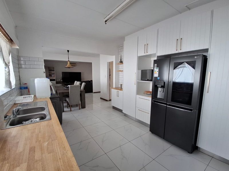 Open-plan kitchen and dining area featuring modern white cabinetry, butcher block countertops, subway tile backsplash, and polished marble-look floor tiles.