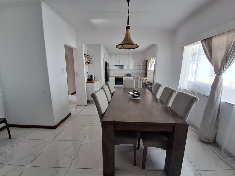 Open-plan dining and kitchen area featuring modern white cabinetry, subway tile backsplash, built-in oven, and light-colored tiled flooring throughout.