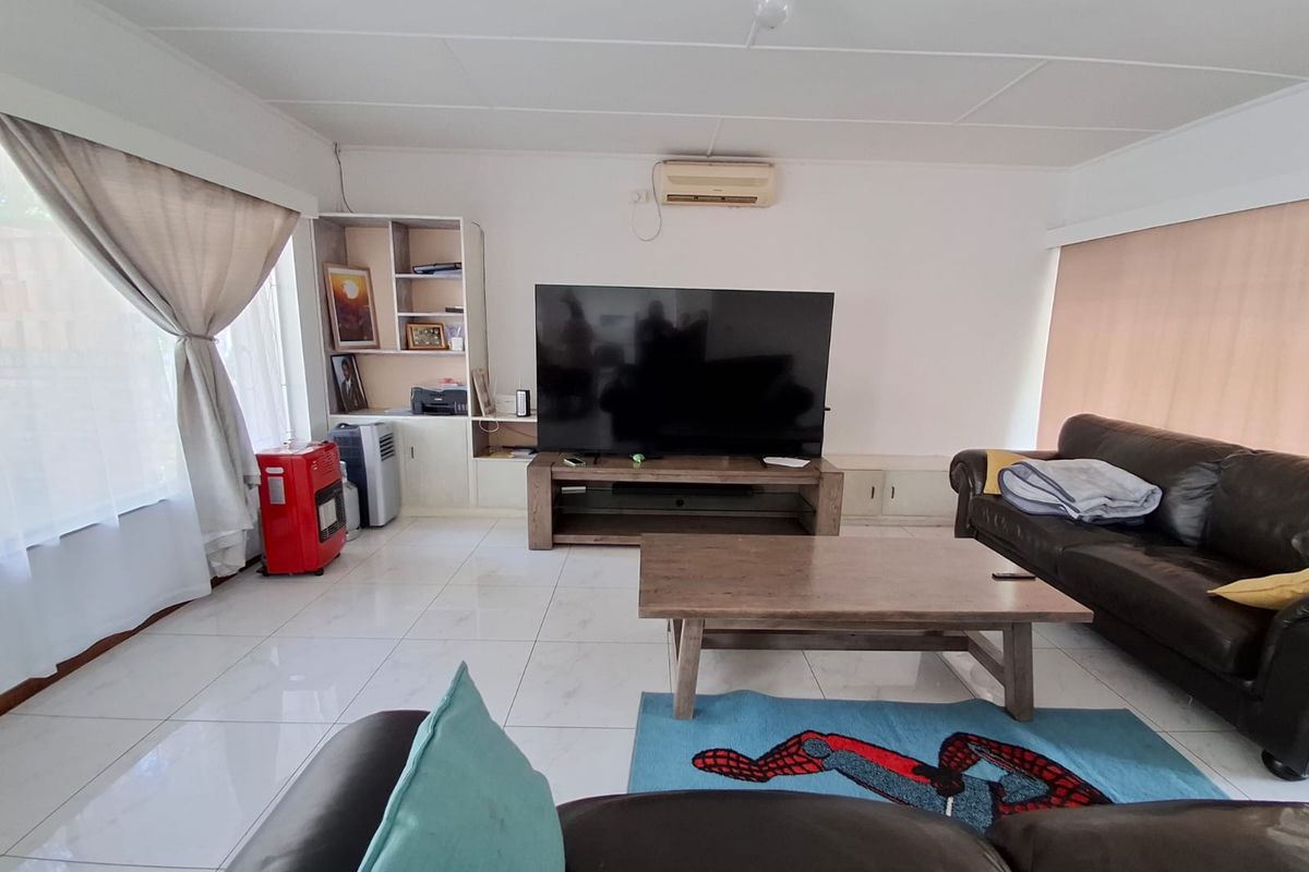 A spacious living room featuring white tiled flooring, a built-in shelving unit, and a wall-mounted split-system air conditioner.