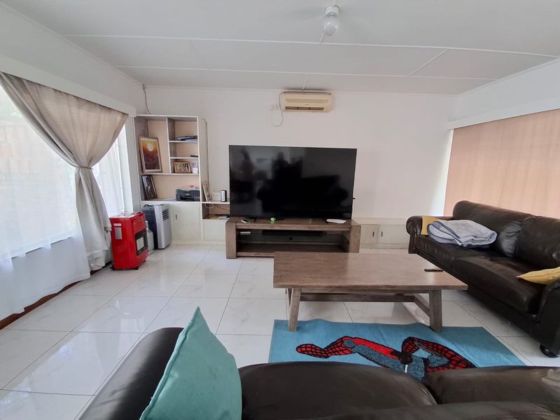 A spacious living room featuring white tiled flooring, a built-in shelving unit, and a wall-mounted split-system air conditioner.