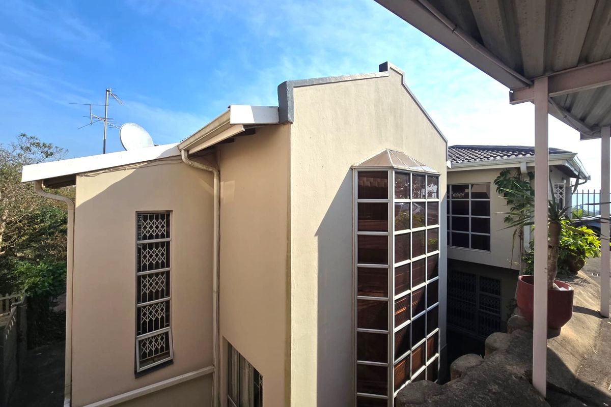 Rear exterior view of the house featuring a prominent bay window, security bars on windows, and a covered patio area.