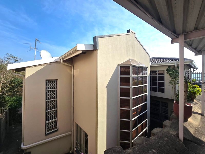 Rear exterior view of the house featuring a prominent bay window, security bars on windows, and a covered patio area.