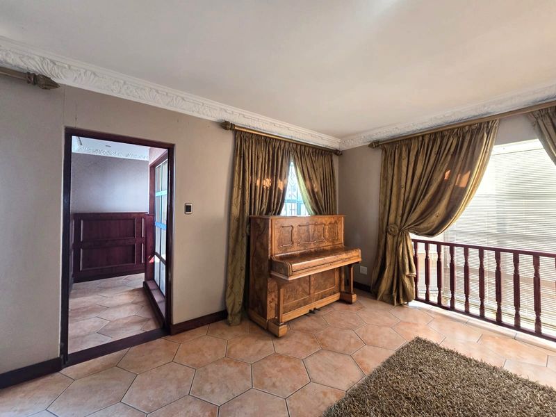 A living area featuring decorative ceiling cornices, terracotta hexagonal floor tiles, and a wooden balustrade overlooking an adjacent space.