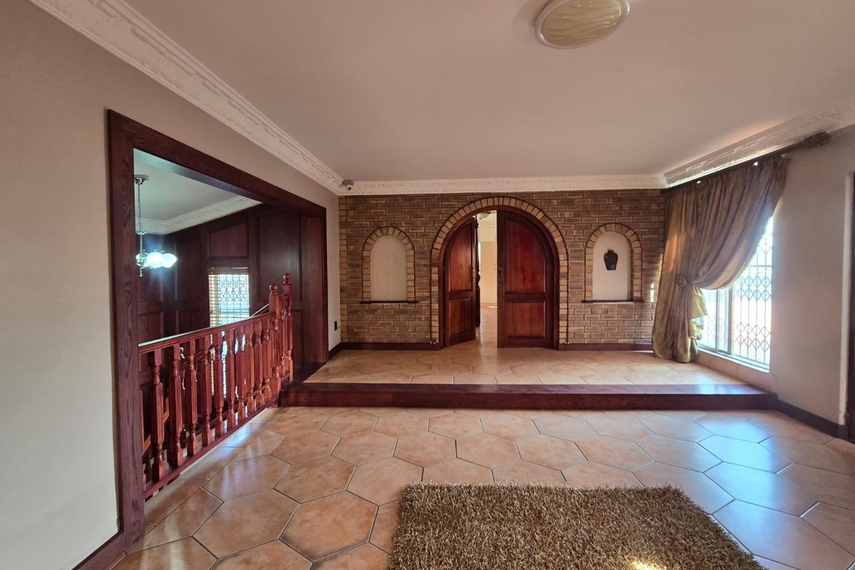 Spacious living area featuring unique hexagonal floor tiles, exposed brick walls with arched doorways, and a classic wooden balustrade overlooking the lower level.