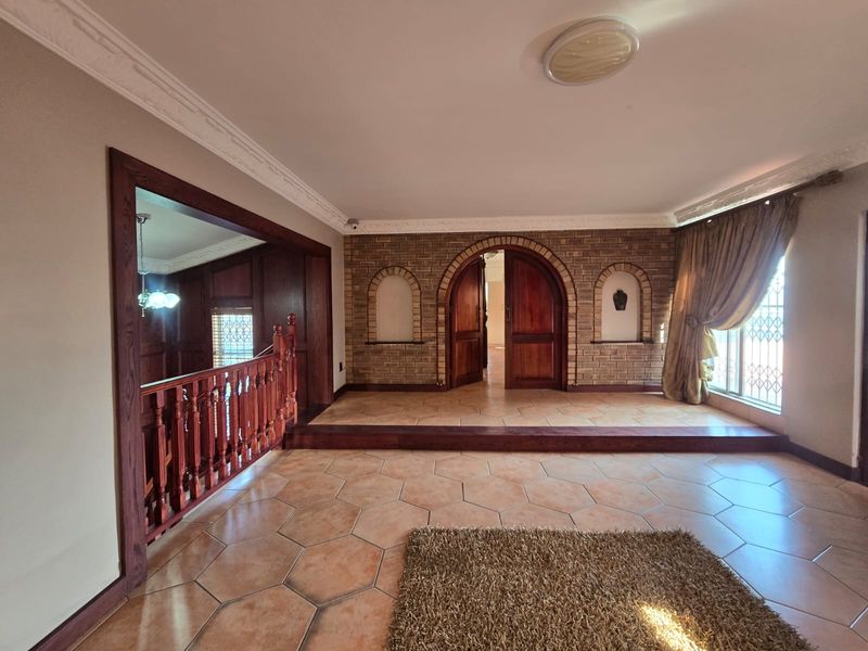 Spacious living area featuring unique hexagonal floor tiles, exposed brick walls with arched doorways, and a classic wooden balustrade overlooking the lower level.