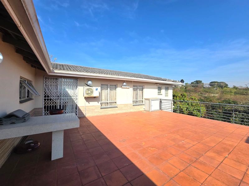 Spacious elevated patio featuring terracotta tiling, a built-in stone counter, and metal balustrades, offering an open outdoor entertainment area.