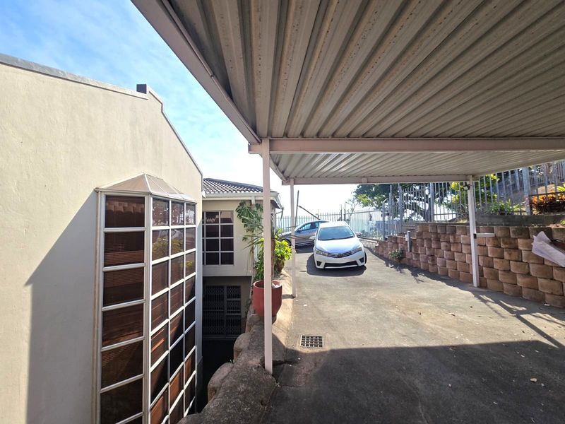Exterior view of the property featuring a covered carport, asphalt driveway, and tiered retaining wall structure.
