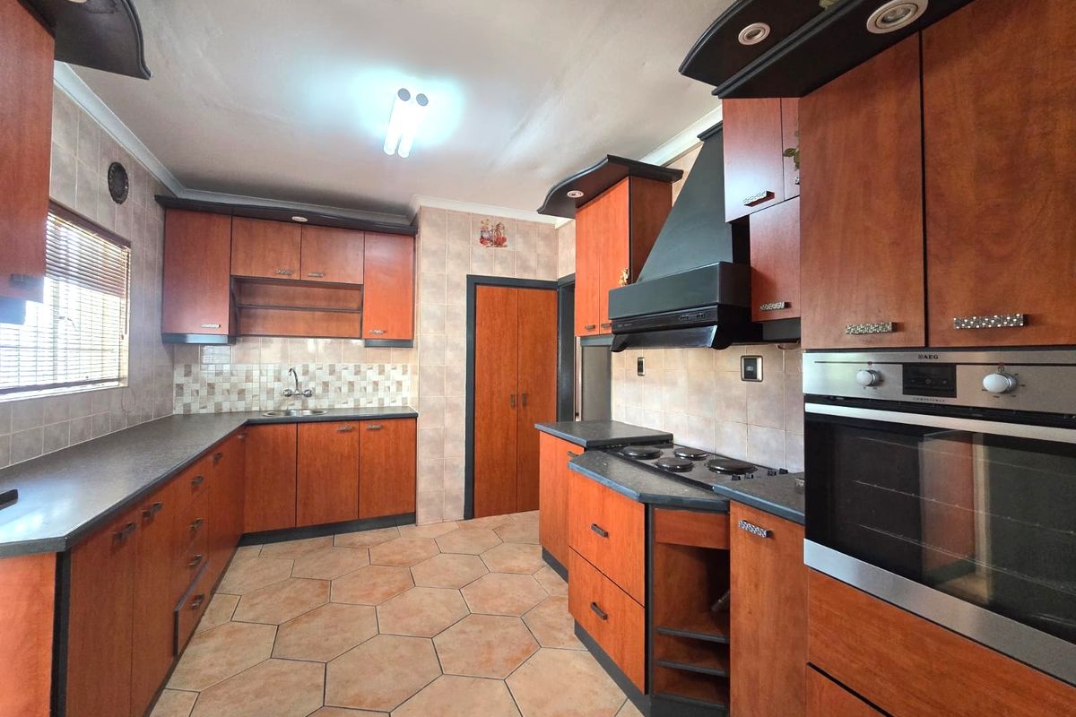 A functional kitchen featuring wood-finish cabinetry, built-in oven and hob, tiled backsplash, and durable tiled flooring with ample counter space.