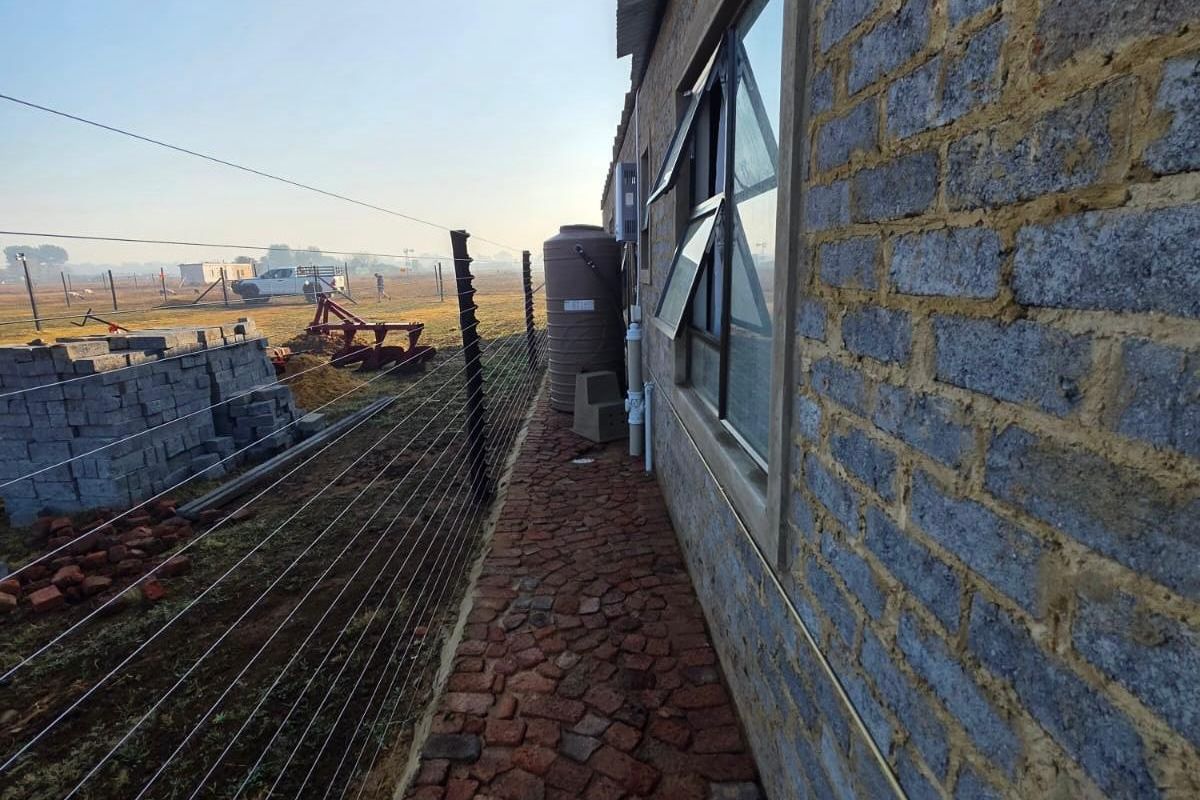Rear exterior view of the property featuring exposed brick walls, a cobblestone pathway, water storage tank, and perimeter electric fencing.