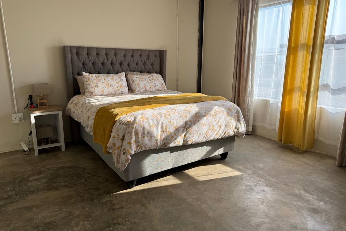 A bedroom featuring polished concrete flooring and exposed electrical conduit, offering a minimalist industrial aesthetic with natural light from the window.