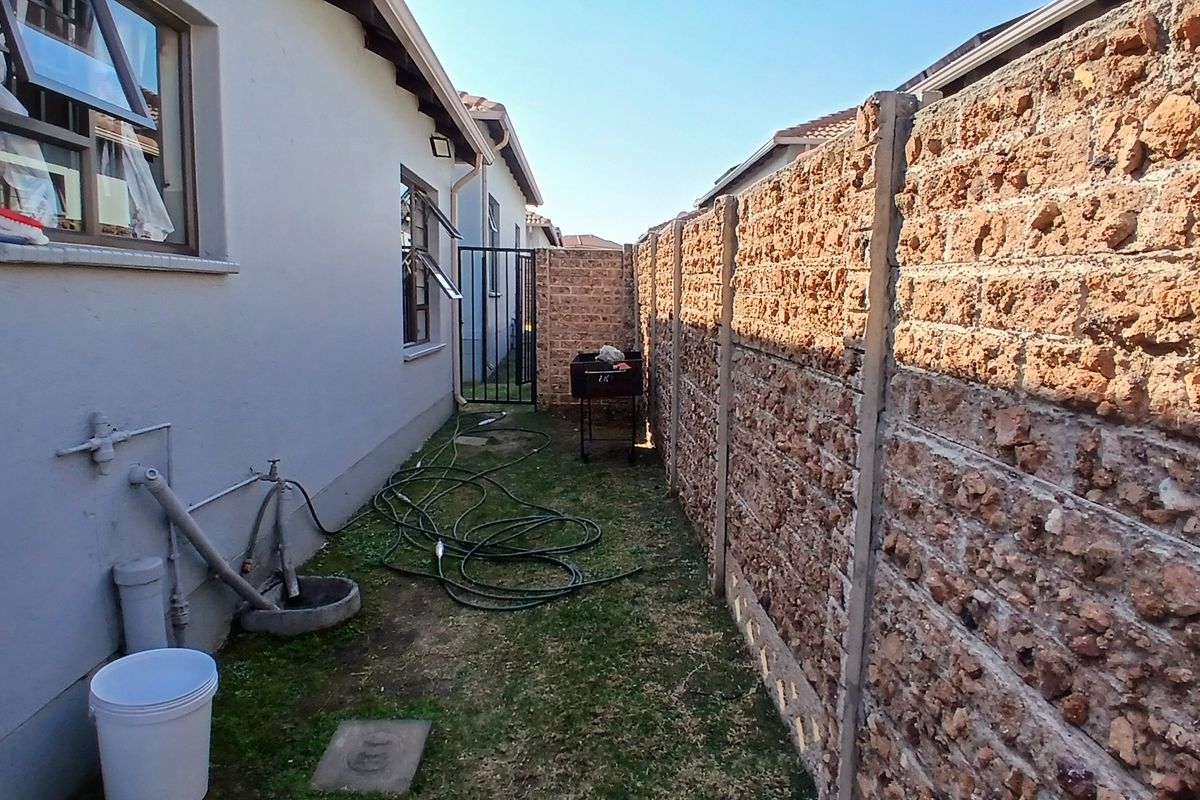 A narrow rear exterior side passage featuring a precast concrete boundary wall, external water tap, and access to the property via a metal gate.