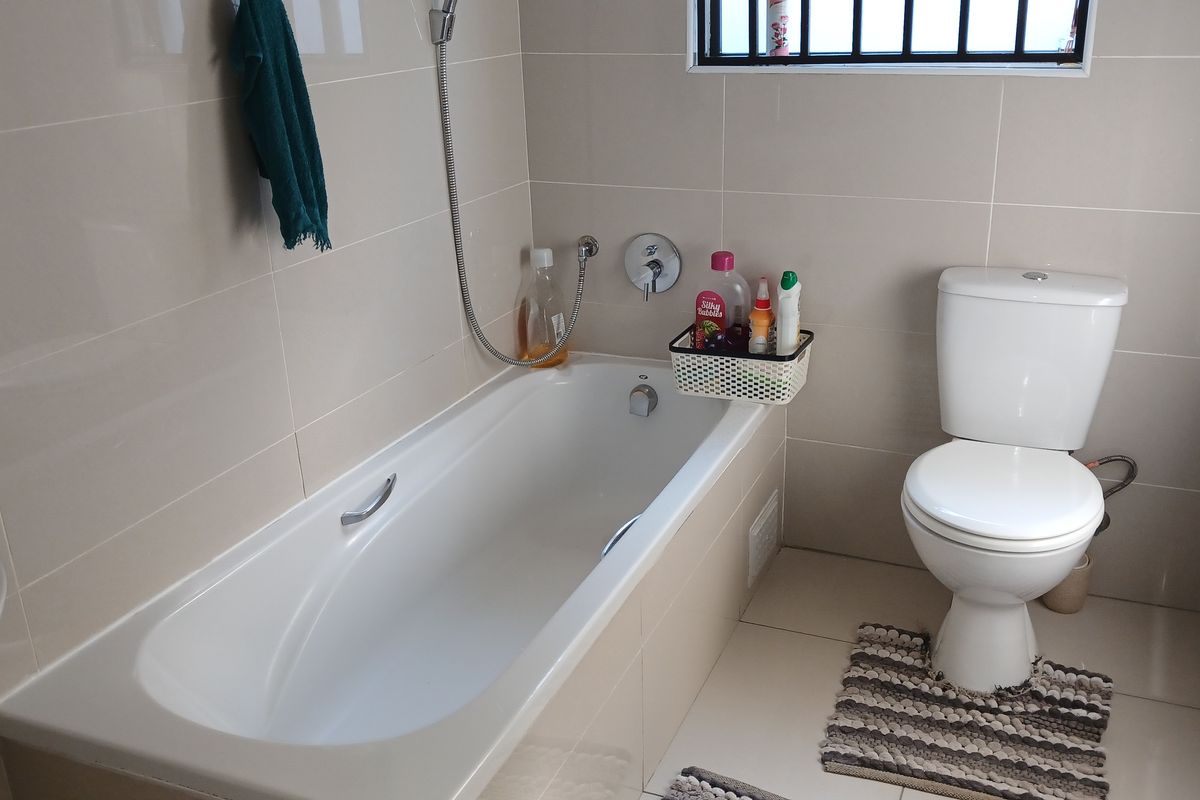 A functional bathroom featuring a built-in bathtub, a standard toilet, and neutral wall tiling with a window for natural light.