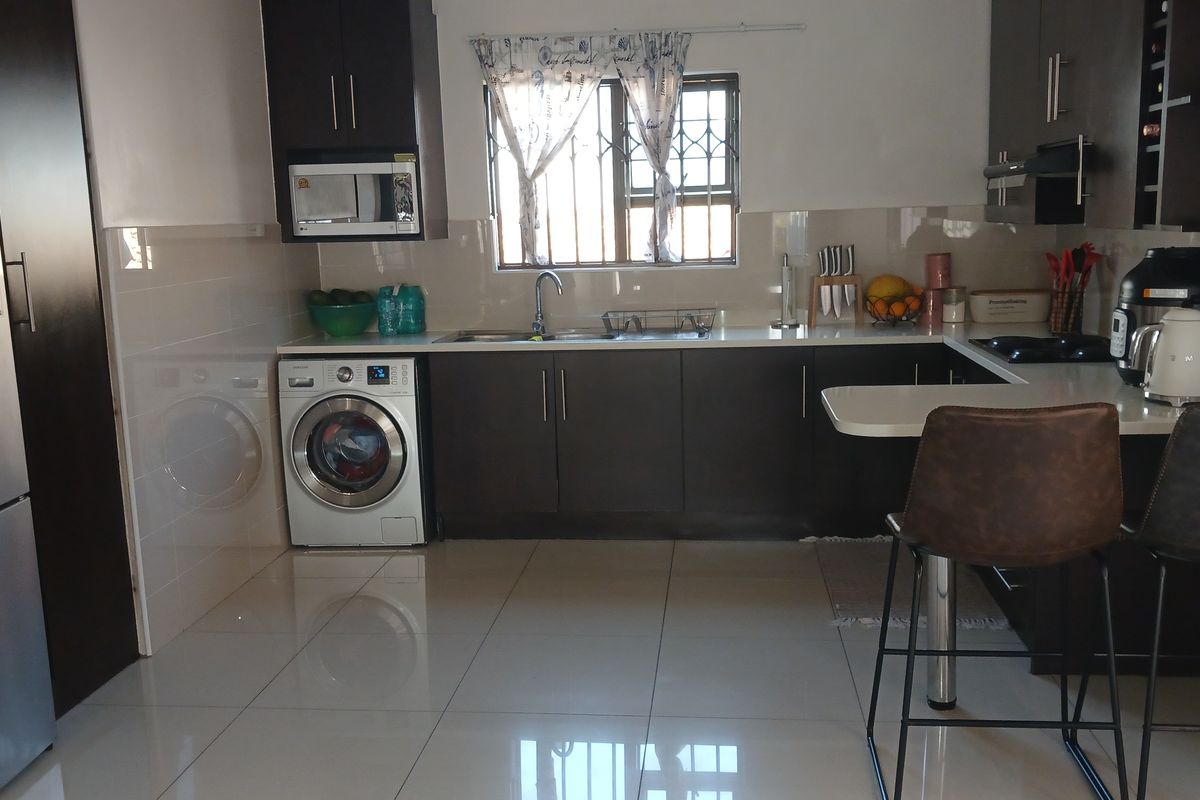 A functional kitchen featuring dark cabinetry, tiled flooring, a breakfast bar, and integrated appliances, offering a clean and practical workspace.