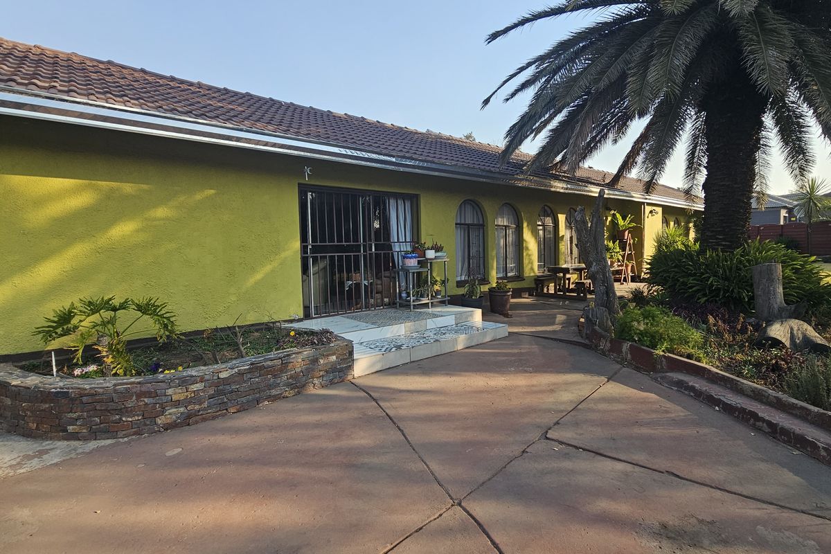 Rear view of the house featuring a concrete patio, stone-clad planter, and arched windows under a tiled roof.