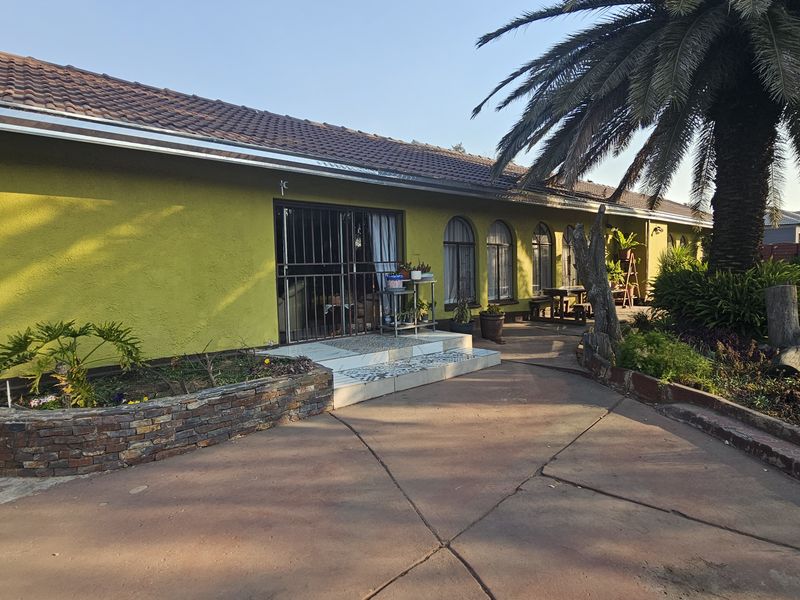 Rear view of the house featuring a concrete patio, stone-clad planter, and arched windows under a tiled roof.