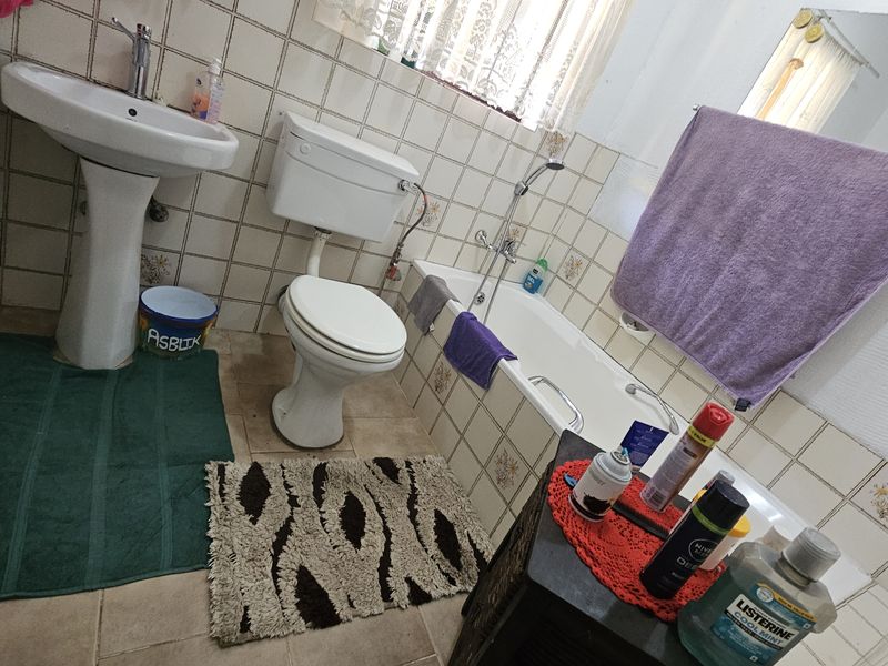 A functional bathroom featuring a pedestal basin, toilet, and bathtub with wall tiling throughout.