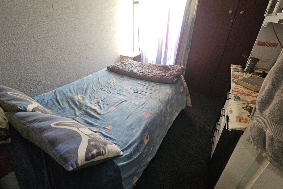 A compact bedroom featuring dark carpet flooring and a built-in wardrobe, providing functional storage space.